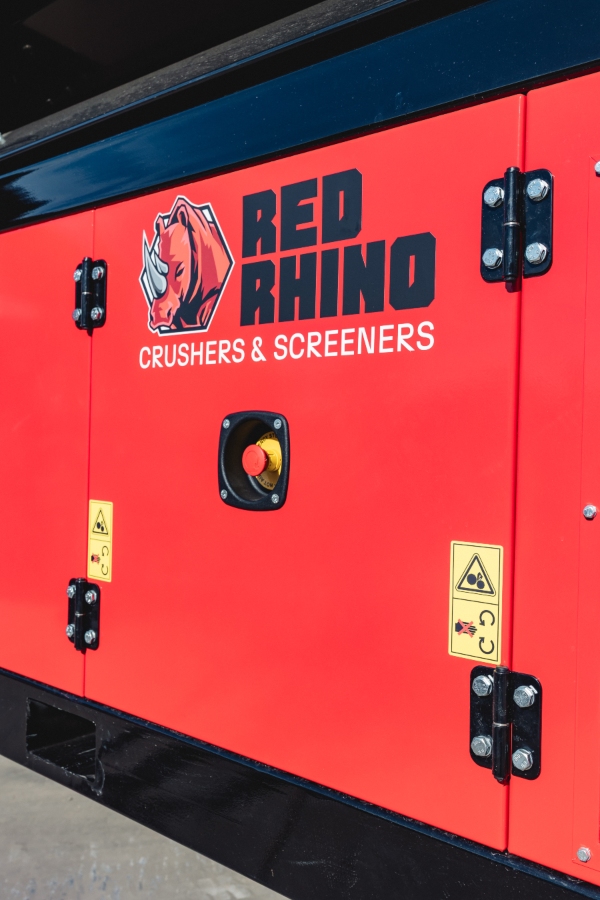 Close-up of the Red Rhino Electric Trommel's bright red panel, showing the 'RED RHINO CRUSHERS & SCREENERS' logo, and a black emergency stop button surrounded by a yellow guard.
