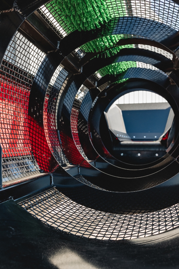 Interior close-up view looking down the length of the Red Rhino Electric Trommel's cylindrical mesh screen, showing the tunnel perspective, the vibrant green cleaning brush inside, and the red main housing on the left.