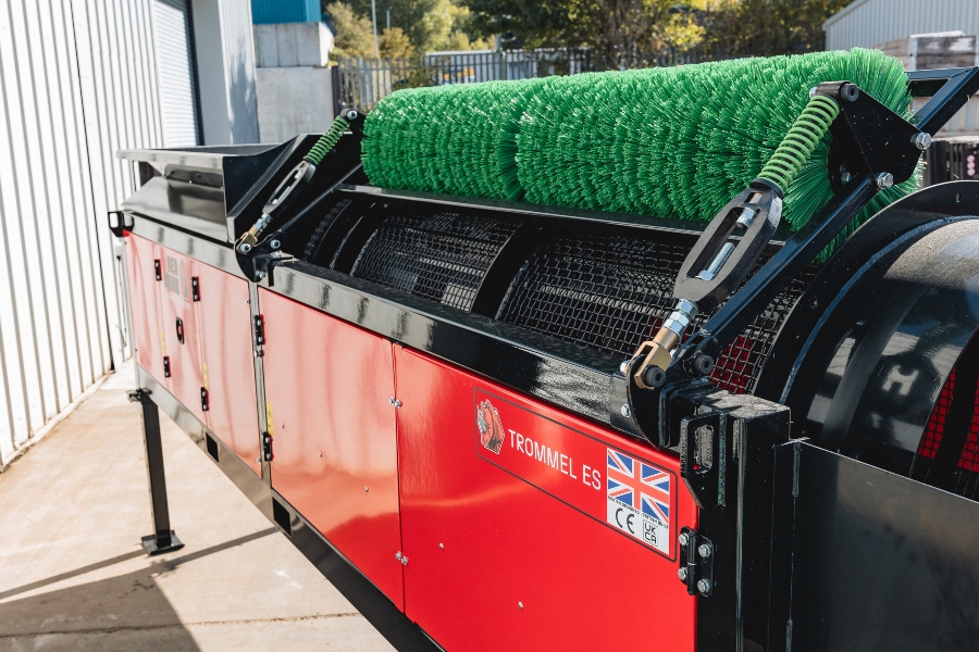 Close-up side view of the Red Rhino Electric Trommel, focusing on the red main housing with the 'TROMMEL ES' decal, the black frame, and the bright green spring-tensioned cleaning brush resting on the mesh screening drum